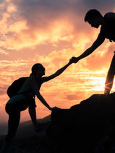 Two hikers helping each other during a sunset climb.