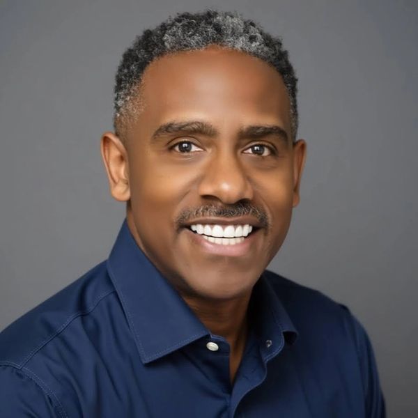 Smiling man with salt-and-pepper hair wearing a blue shirt against a gray background.