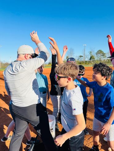 Coach and kids celebrating with high fives on a baseball field.