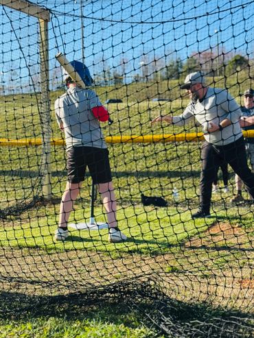 A child practicing baseball with a coach in a batting cage.