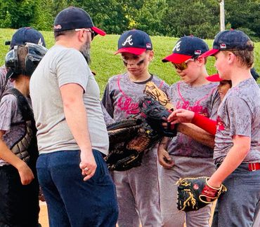 Youth baseball team huddles with coach on pitcher's mound.