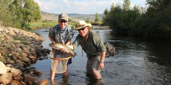 Two men fishing in a river, proudly holding a large fish.