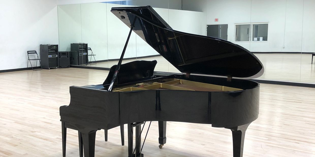 Black grand piano in a spacious room with mirrors.