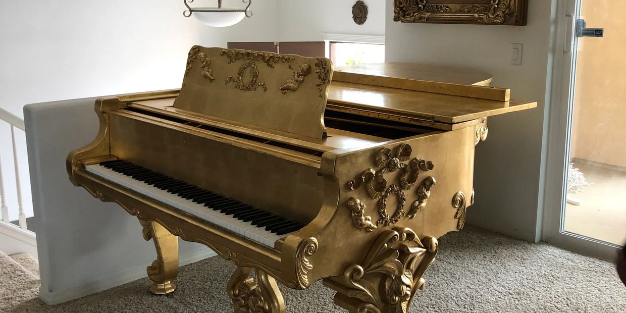 Golden grand piano with ornate carvings in a living room.