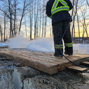 Worker using a steam cleaner on wooden planks outdoors in winter.
