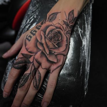 Custom black and grey realism rose tattoo with leaf accents on hand, Mayhem Tattoo in Salem, NH.
