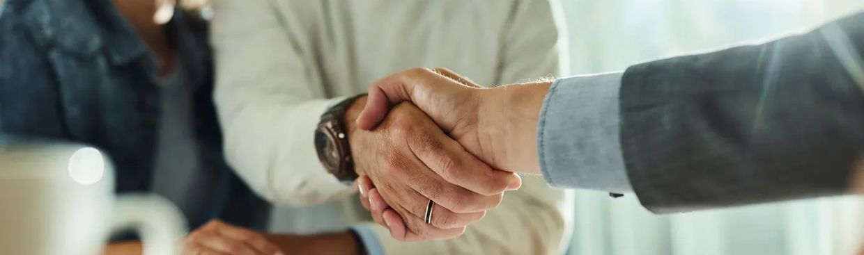 Two professionals shaking hands across a desk in a business setting