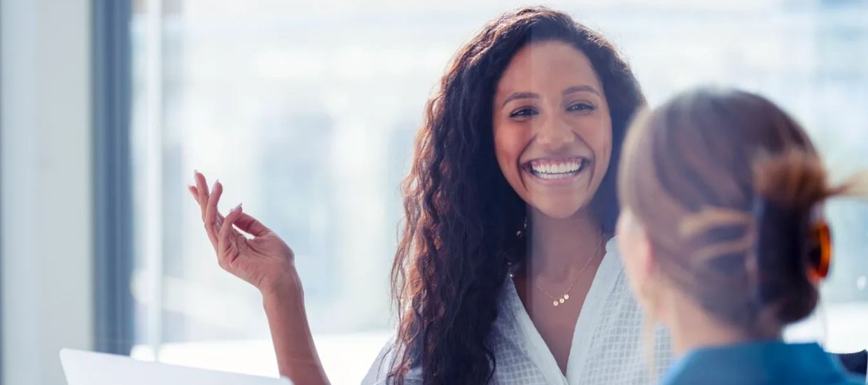 Two people in conversation at a table, one person smiling and gesturing while speaking