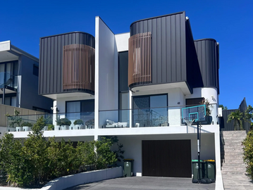 Modern twin houses with curved balconies and a basketball hoop in front.