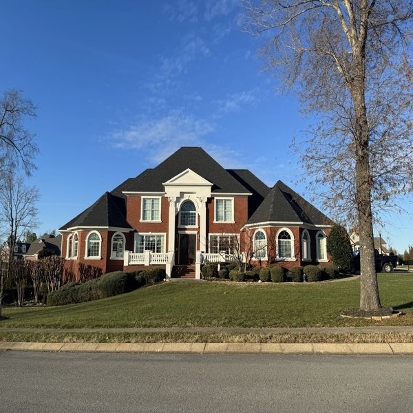 Large brick house with a manicured lawn under a clear blue sky.