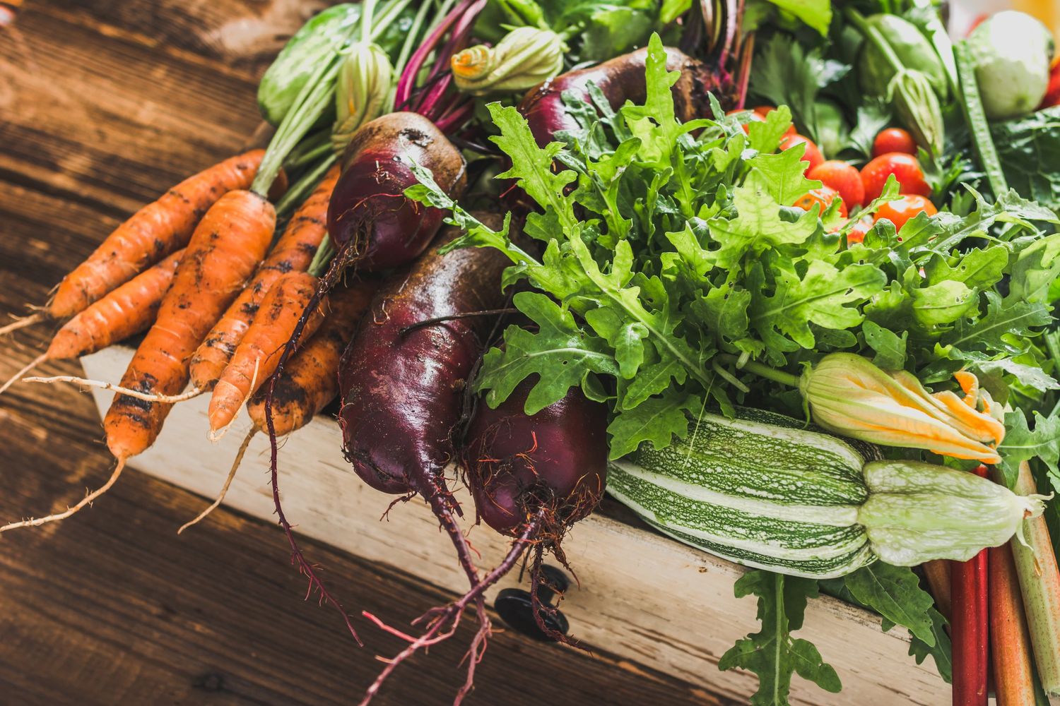 A stock image shows carrots, beets, lettuce, zucchini, and other vegetables in a wood box basket.