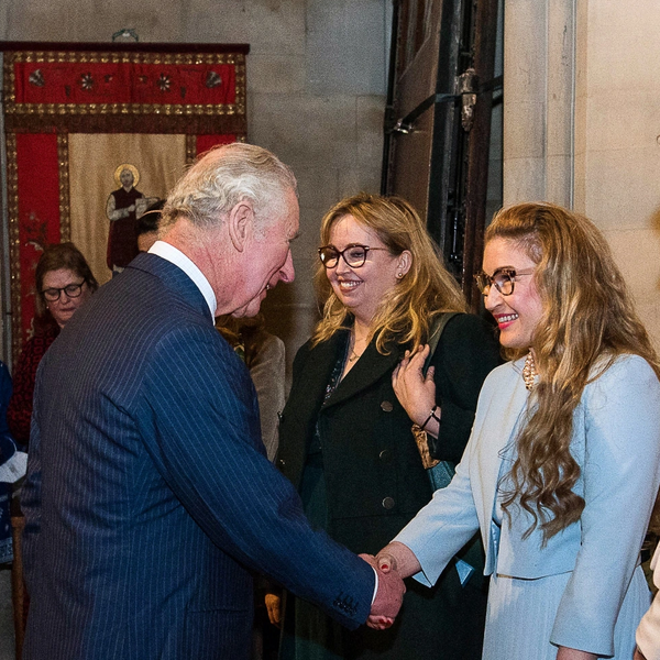 A man in a suit shakes hands with a smiling woman in a light blue outfit indoors.
