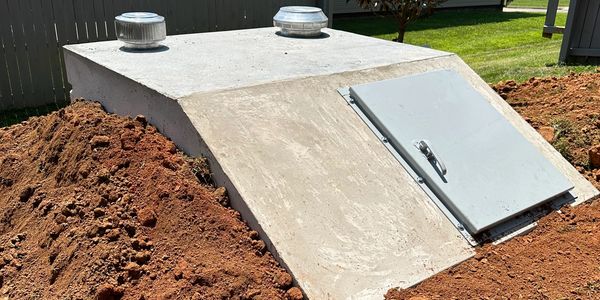 a concrete storm shelter with dirt around it with a house in the back of it