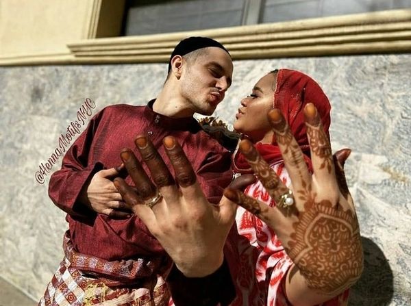 A couple in traditional attire showing hands with henna and wedding rings.