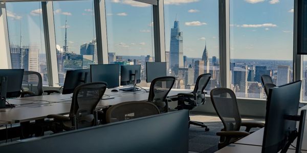 Modern office with empty desks and city skyline view through large windows.