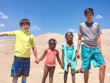 Four kids holding hands and smiling at the beach on a sunny day.