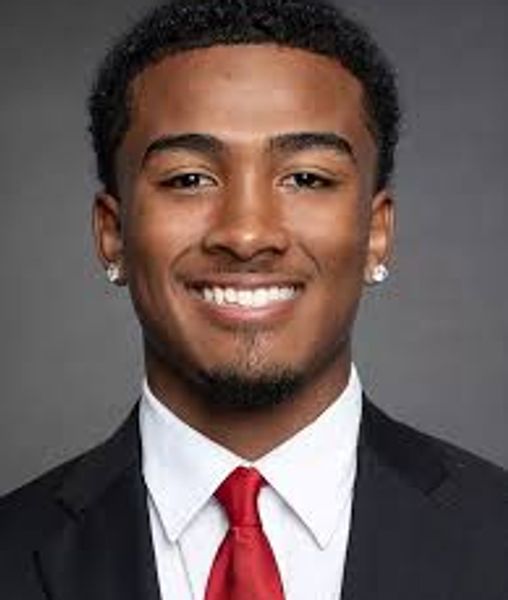 Smiling young man in suit and red tie against gray background.