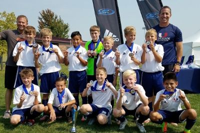 Youth soccer team proudly displays medals and a trophy outdoors.