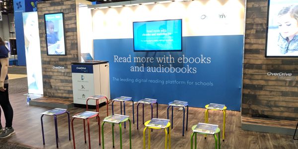 Booth promoting ebooks and audiobooks with colorful stools and digital displays.