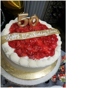 A beautifully decorated strawberry 2-tier cake with white frosting and a gold ribbon across the cake.