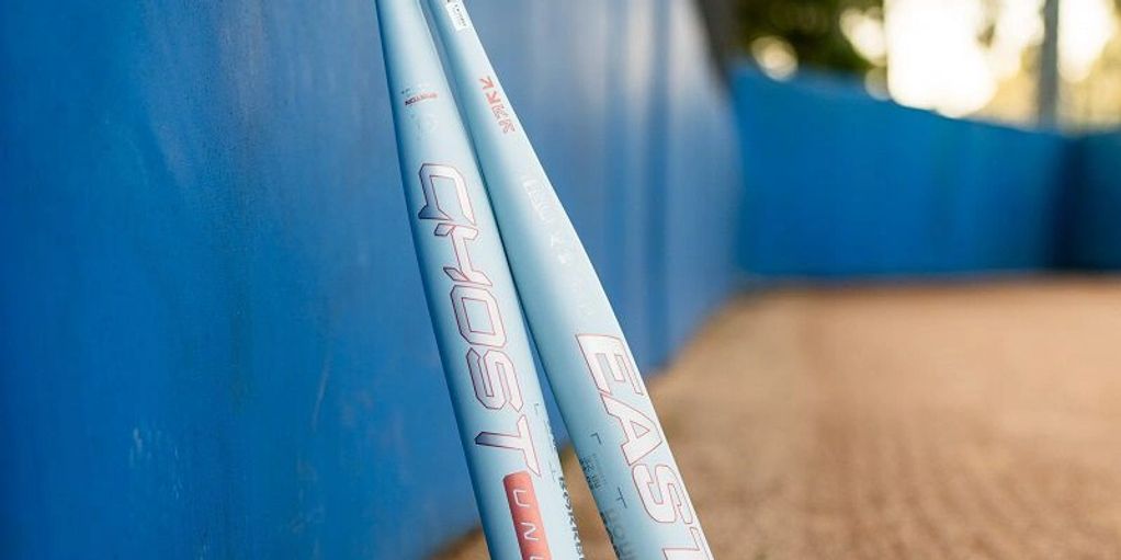 Two light blue baseball bats leaning against a blue wall on a baseball field.