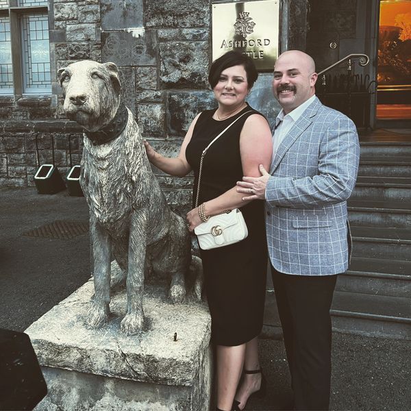 A couple posing by a dog statue outside Ashford Castle.