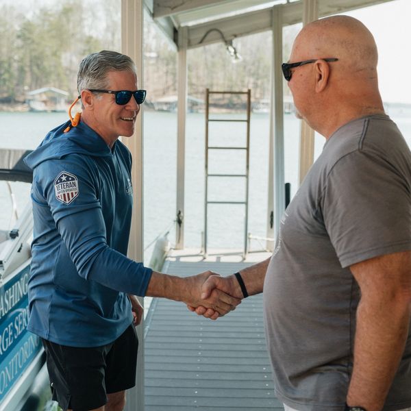 Two men shaking hands on a dock near water.