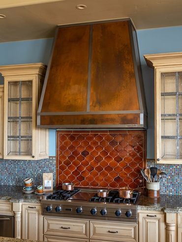 Custom copper kitchen range hood by Tin Works with warm patina finish and metal trim