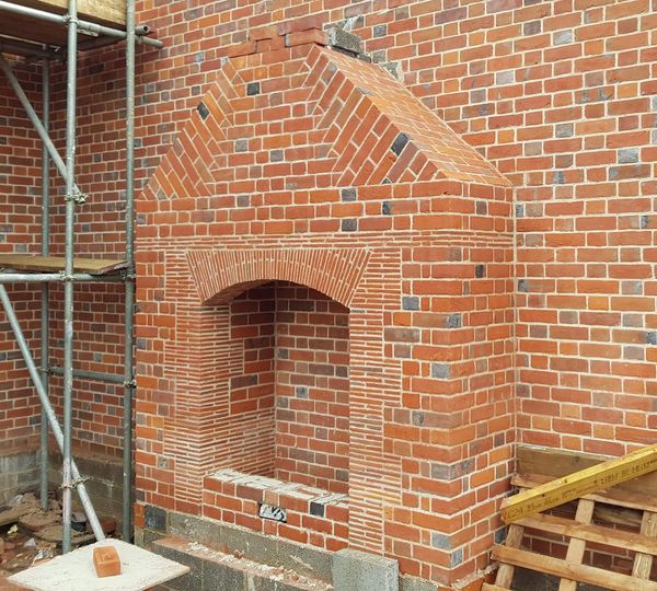 A partially built brick fireplace with scaffolding and construction materials nearby.
