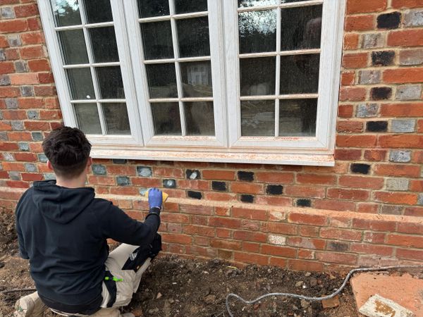 Person repairing brick wall beneath a window.