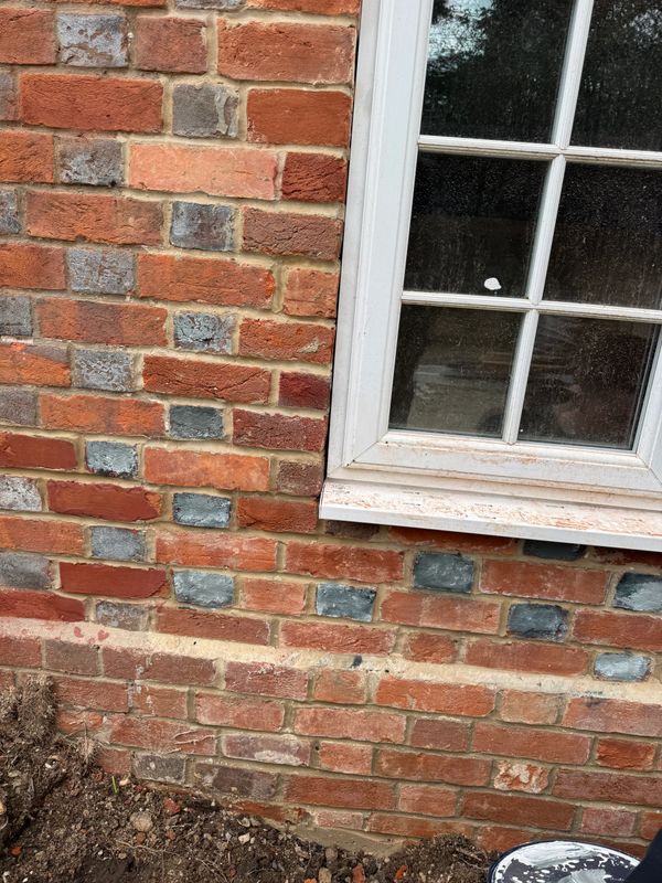 A brick wall with mixed red and gray bricks beside a white window.