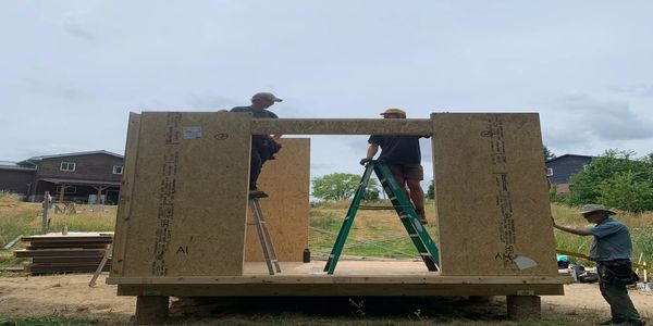 Three people assembling a wooden structure on ladders outdoors.