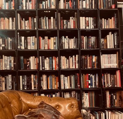 A cozy library wall filled with books and a brown leather couch.