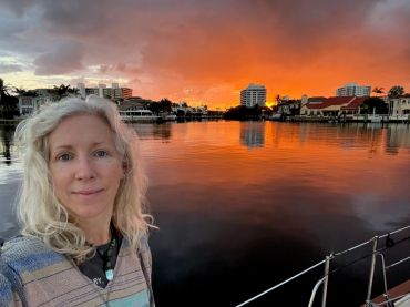Woman taking a selfie with a stunning orange sunset over a waterfront cityscape.
