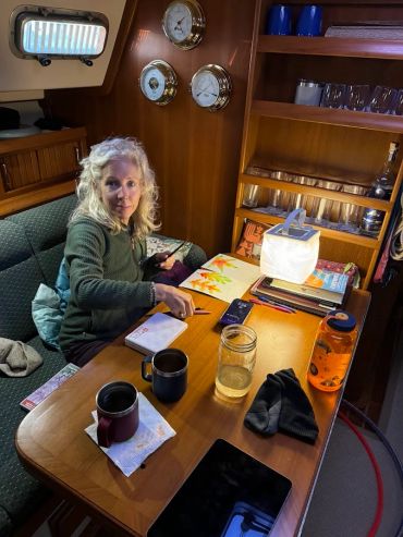 Woman painting autumn leaves inside a cozy boat cabin.