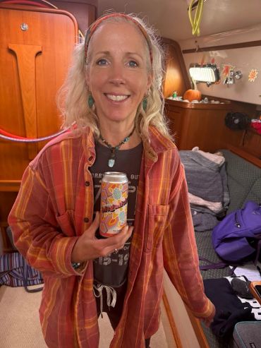 Smiling woman in a cozy boat cabin holding a colorful can of beverage.