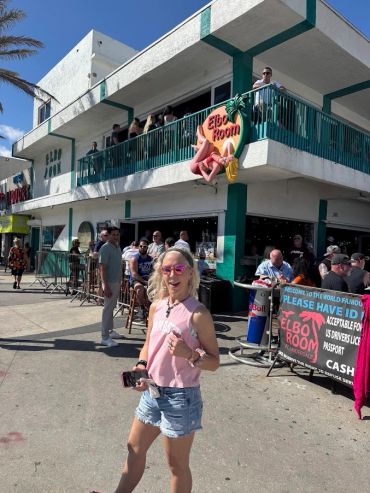 Woman in pink tank top and shorts outside Elbo Room bar on a sunny day.