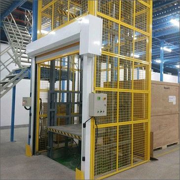 Industrial freight elevator with yellow safety cage in a warehouse.