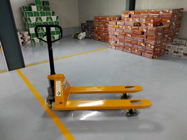 A yellow pallet jack in a warehouse with stacked boxes.