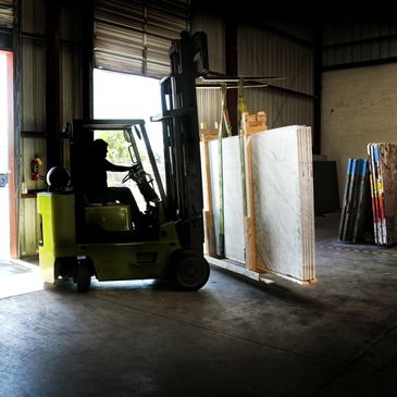 A forklift operator moves large slabs inside a warehouse.