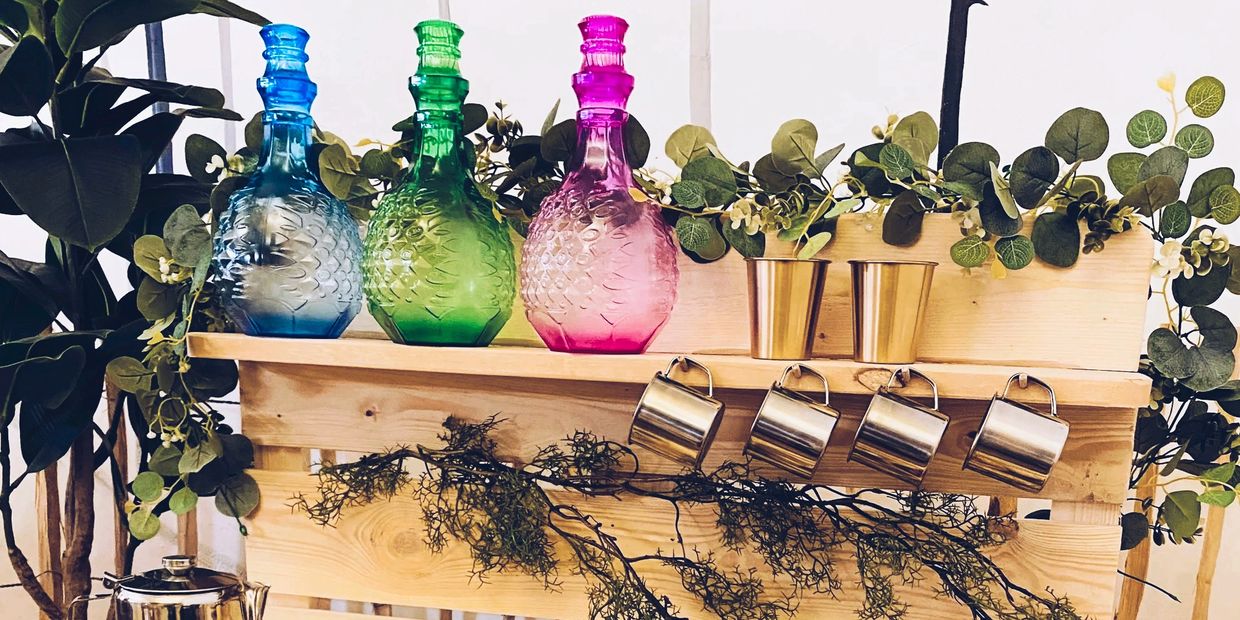 Colorful glass bottles, plants, and kitchen tools on a rustic wooden table and shelf.