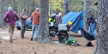 The Cajun Effect, Men stand around a touring motorcycle discussing the art of motorcycle camping wit