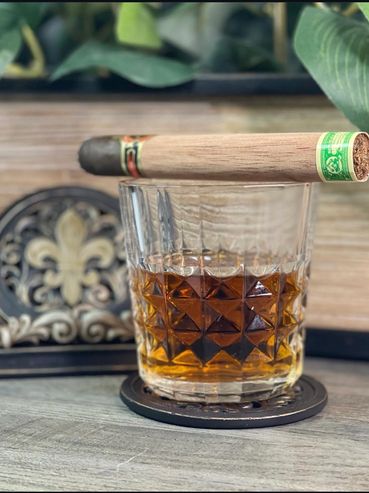 Whiskey glass with a cigar resting on top, set on a coaster.