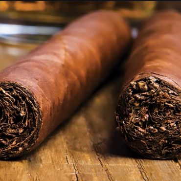 Close-up of two rolled cigars on a wooden surface.