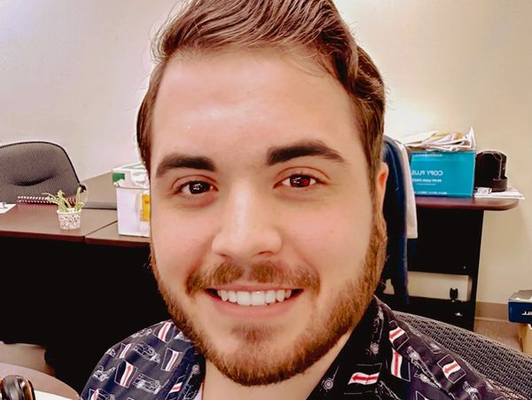 Smiling man with a beard wearing a patterned shirt in an office.
