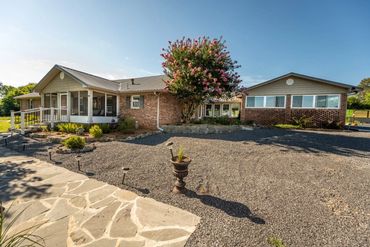 Single-story brick house with gravel yard and blooming tree under clear blue sky.