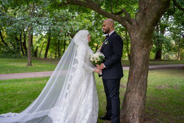 Bride and groom smiling at each other in a lush green park.