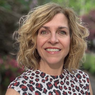Smiling woman with curly hair outdoors in a patterned top.