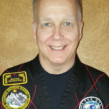 Smiling man in a martial arts uniform with master instructor patches.