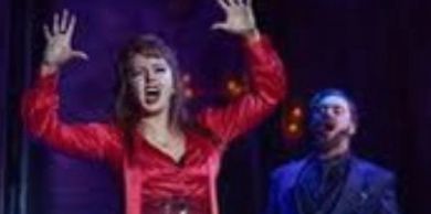 Performer singing with raised hands on stage.